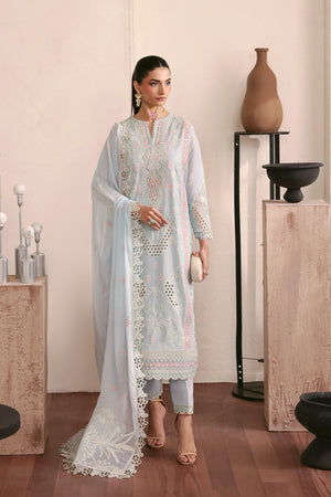 Woman in a light blue embroidered outfit standing in a minimalistic room with decorative elements.