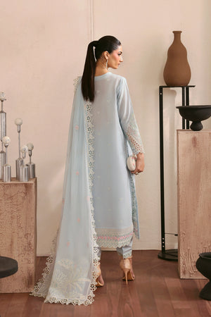 Woman in a light blue traditional outfit with white lace details, standing in a room with decorative items.