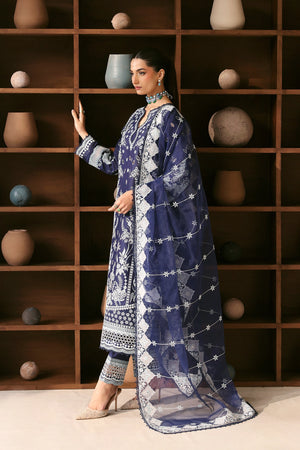 Woman in a blue and white patterned outfit standing in front of a wooden shelf with decorative pots.