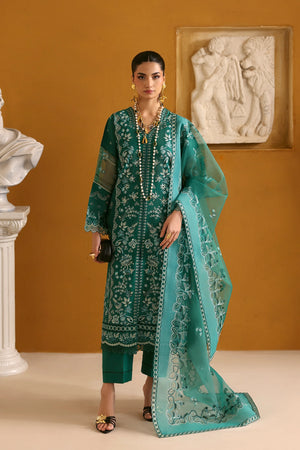 Woman in a teal embroidered outfit standing against an orange wall with classical sculptures.