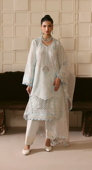 Woman wearing a light blue embroidered traditional outfit in a room with a neutral background.