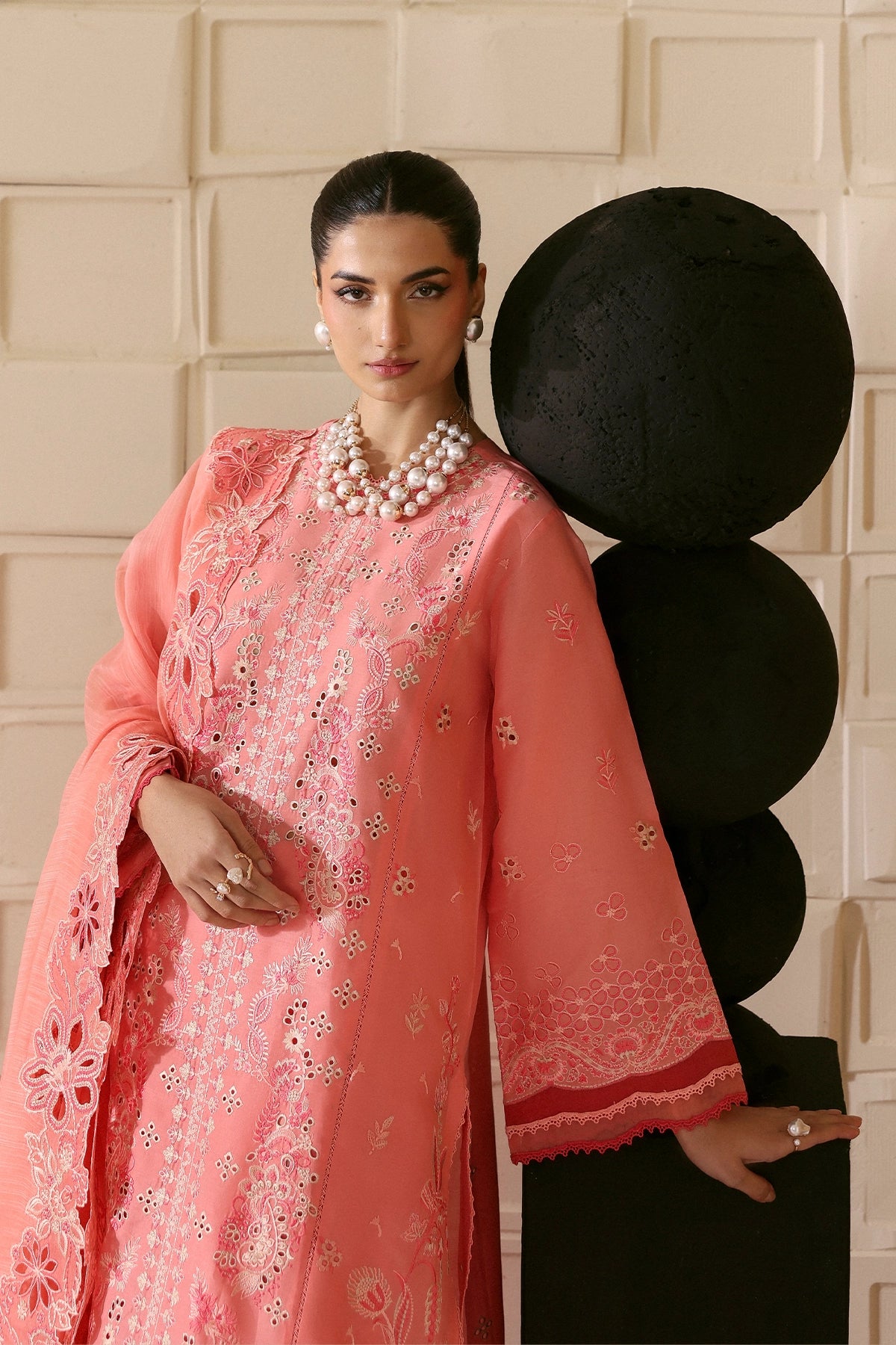 Woman in a pink embroidered traditional outfit standing against a decorative wall.