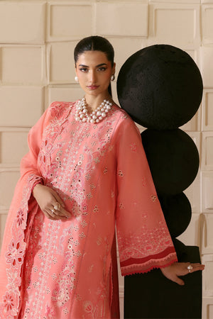 Woman in a pink embroidered traditional outfit standing against a decorative wall.