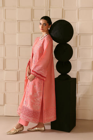 Woman in a pink traditional outfit standing against a textured wall.