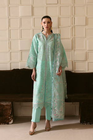 Woman wearing a light blue traditional outfit with intricate patterns in a minimalistic setting.