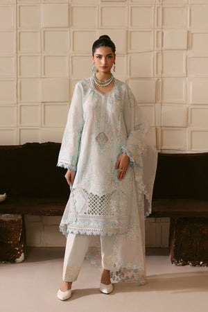 Woman wearing a light blue embroidered outfit with white pants against a neutral background