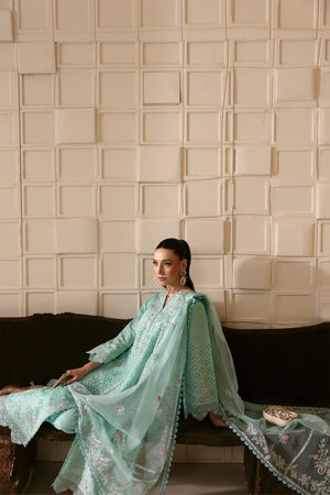 Woman in a light blue embroidered outfit sitting against a textured beige wall.