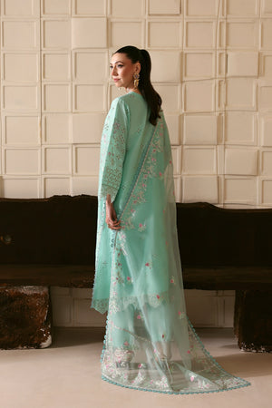 Woman in a light blue embroidered traditional outfit standing against a textured wall.