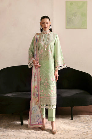 Woman in a light green traditional outfit with a floral dupatta in a room with a black sofa and framed artwork.