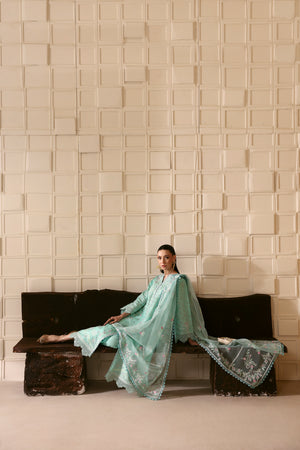 Woman in a light blue traditional outfit sitting on a black bench against a textured beige wall.