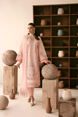 Woman in a light pink embroidered dress standing between stone spheres with a bookshelf in the background.