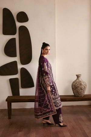 Woman in a purple traditional outfit standing in a room with decorative wall art and a vase.