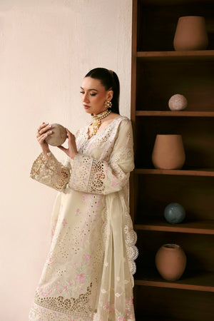 Woman in a white embroidered outfit holding a decorative pot in a room with shelves and vases.