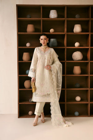 Woman in a white embroidered outfit standing in front of a bookshelf with decorative items.