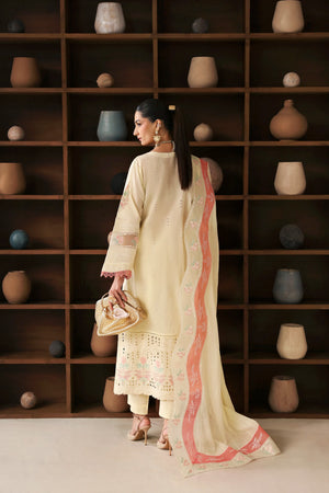 Woman in a cream traditional outfit with a pink border standing in front of a wooden shelf with decorative pots.