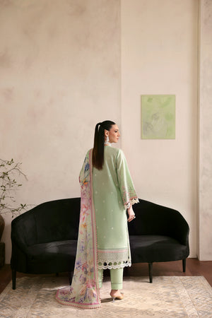 Woman in a light green outfit standing in a room with a black sofa and a painting on the wall.