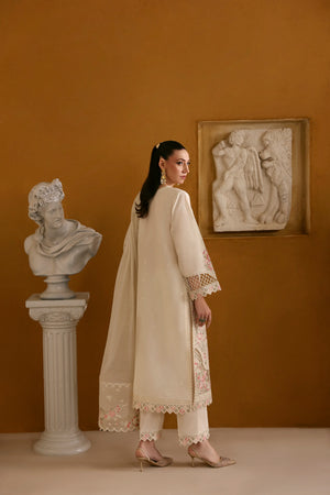 Woman in a cream traditional outfit standing in an elegant room with classical sculptures.