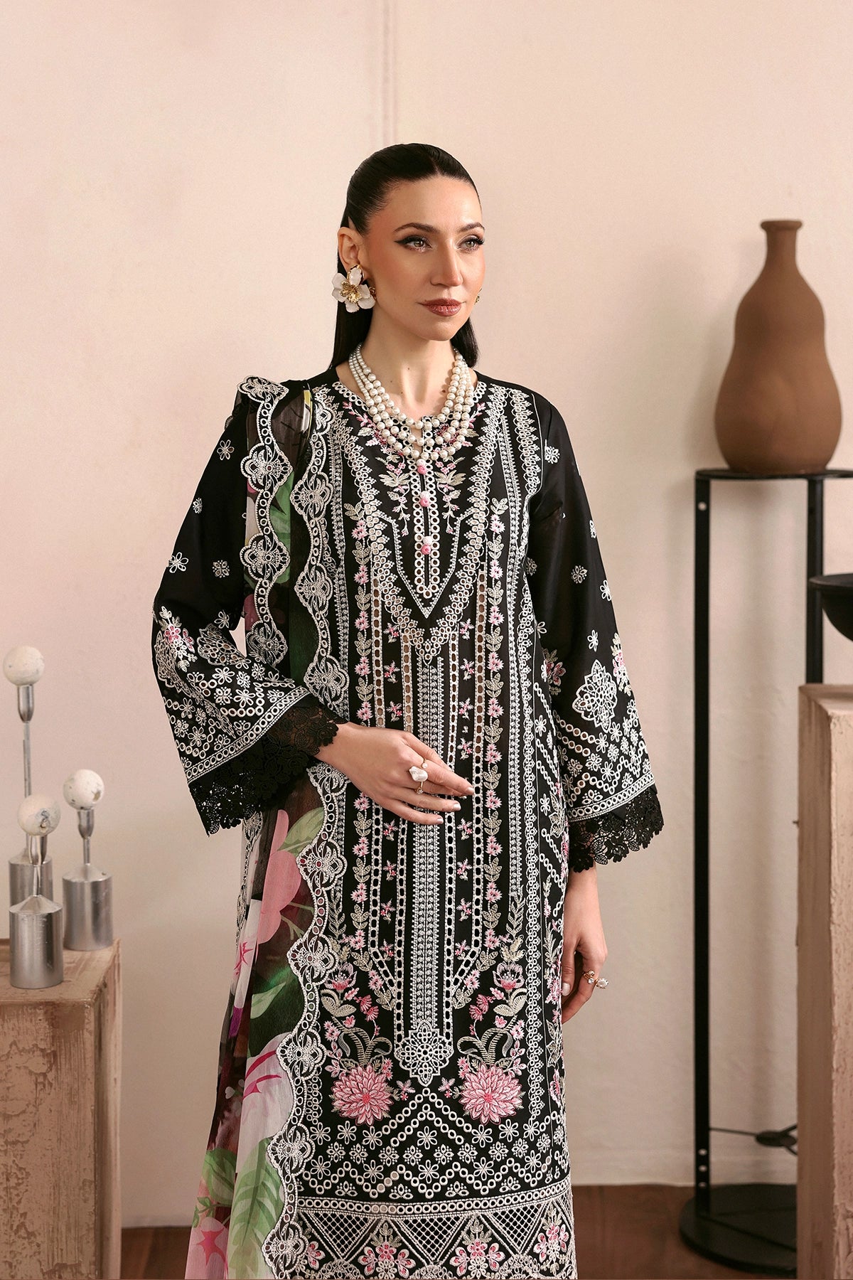 Woman wearing a black and white embroidered dress with floral patterns in a room setting.
