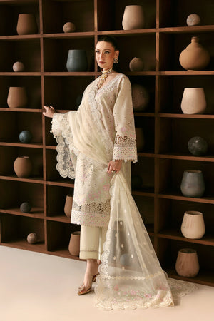 Woman in a white traditional outfit standing in front of a wooden shelf with decorative pots.