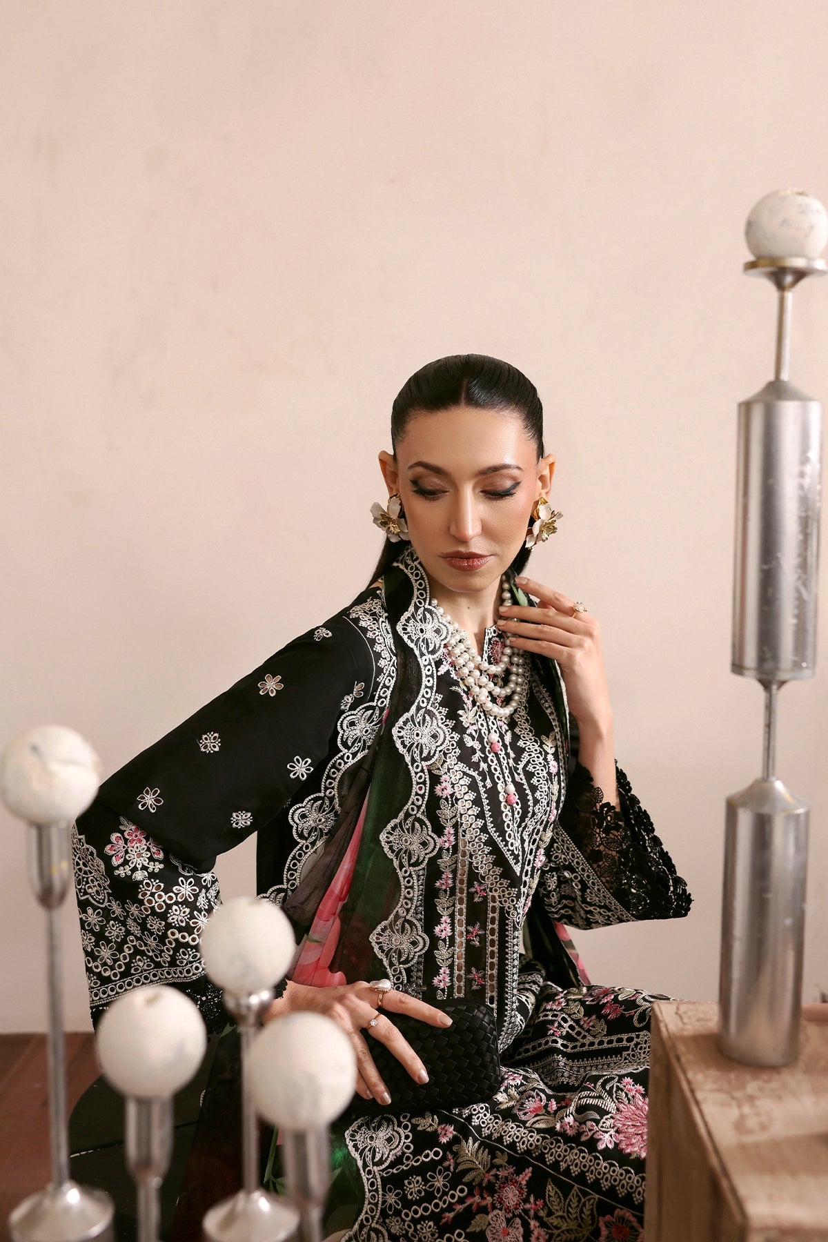 Woman in traditional attire with intricate patterns, standing in a room with decorative elements.