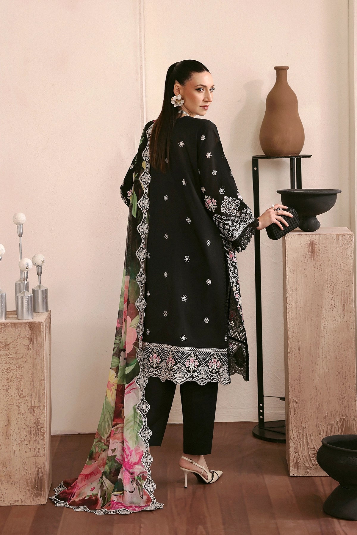 Woman in a black embroidered outfit with a floral scarf in a minimalistic setting