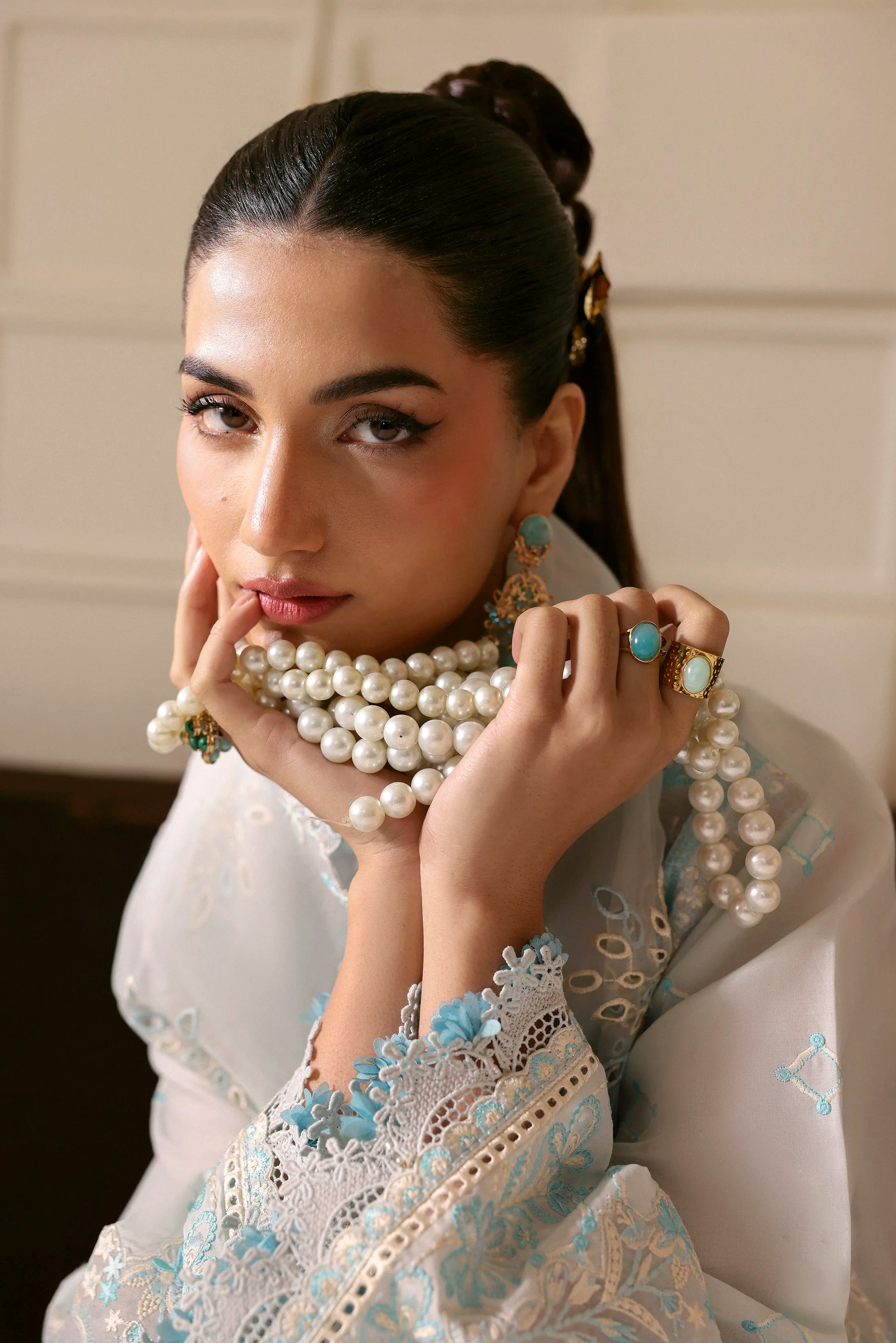 Woman wearing a pearl necklace and jewelry with a neutral background