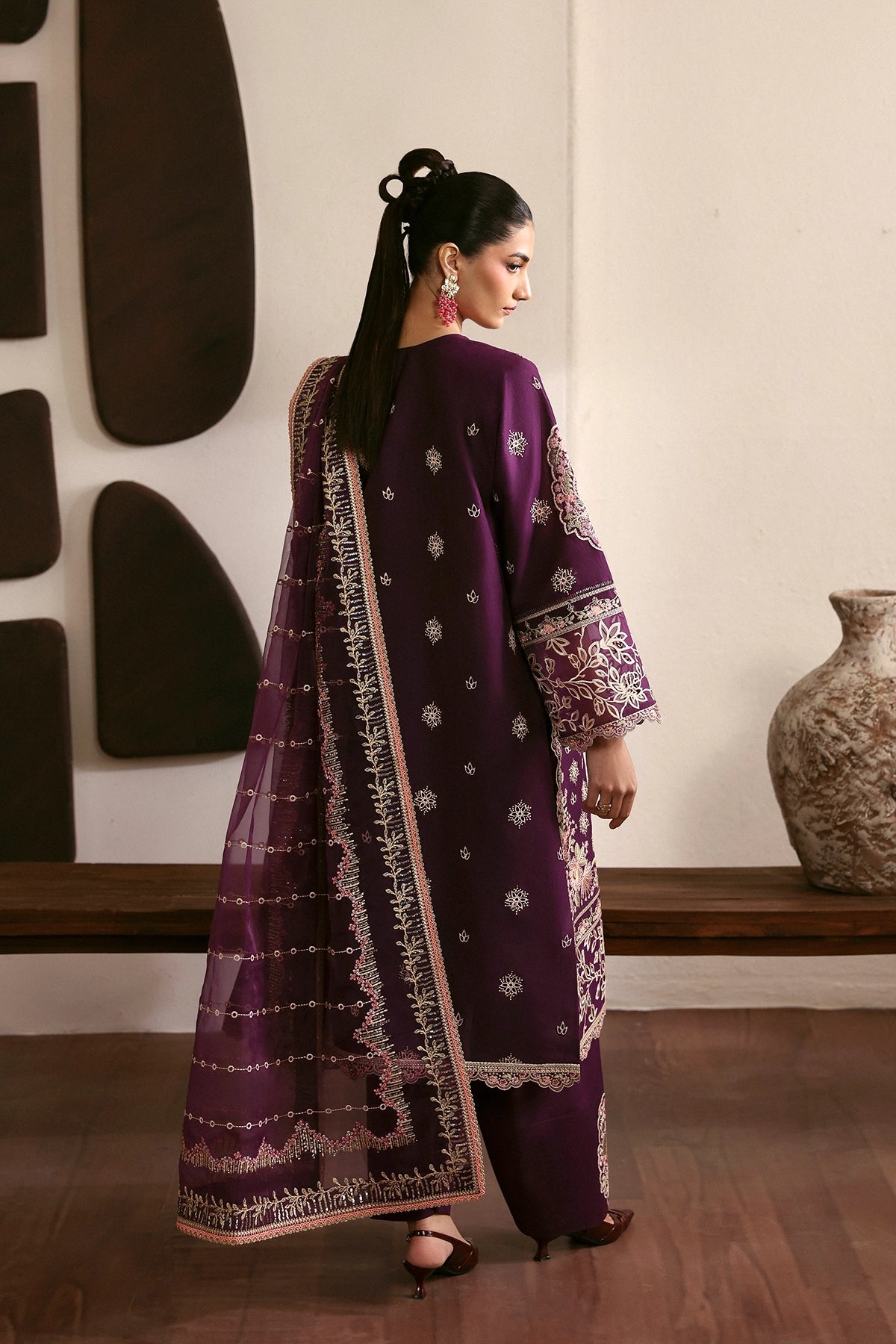 Woman wearing a traditional purple outfit with intricate patterns in a room with decorative elements.