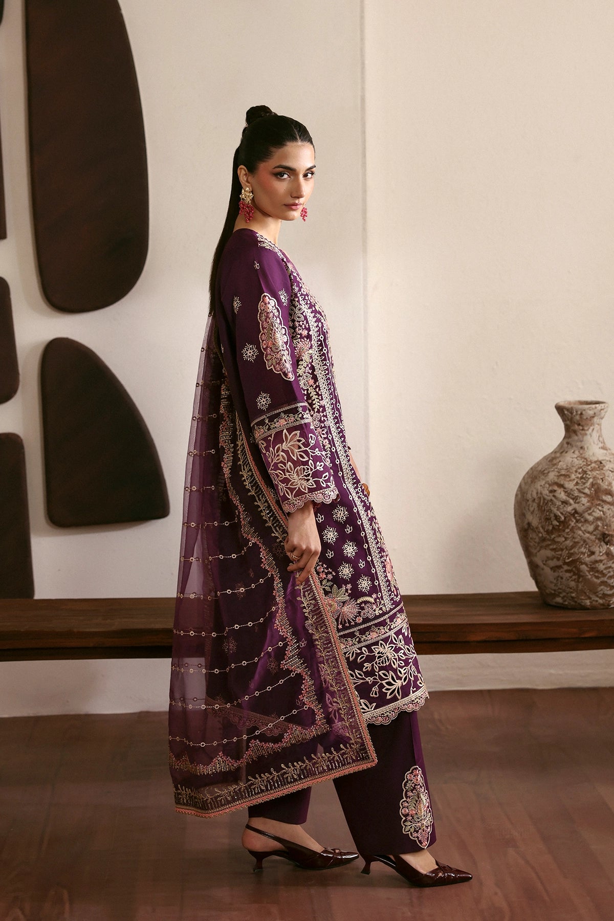 Woman in a purple and white patterned outfit standing in a room with decorative vases.