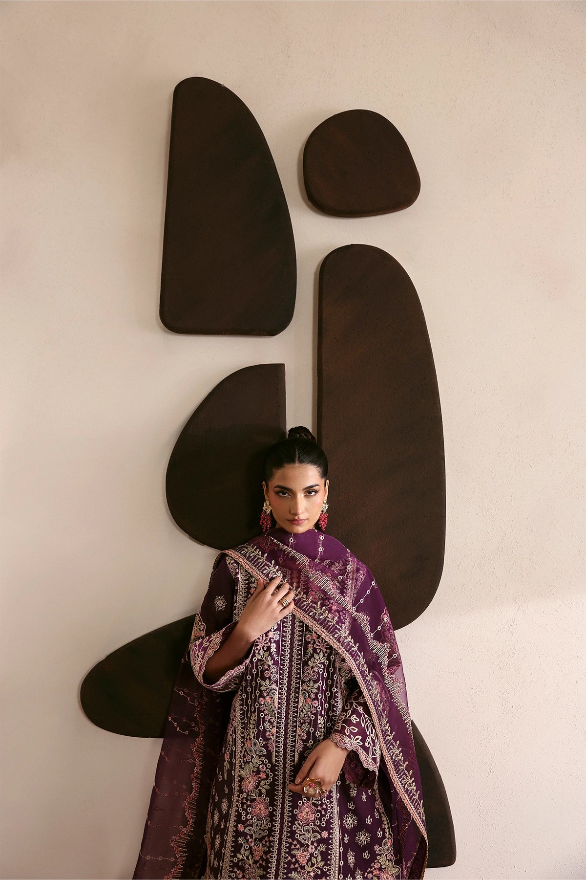 Woman in a patterned outfit standing against a wall with abstract black shapes.