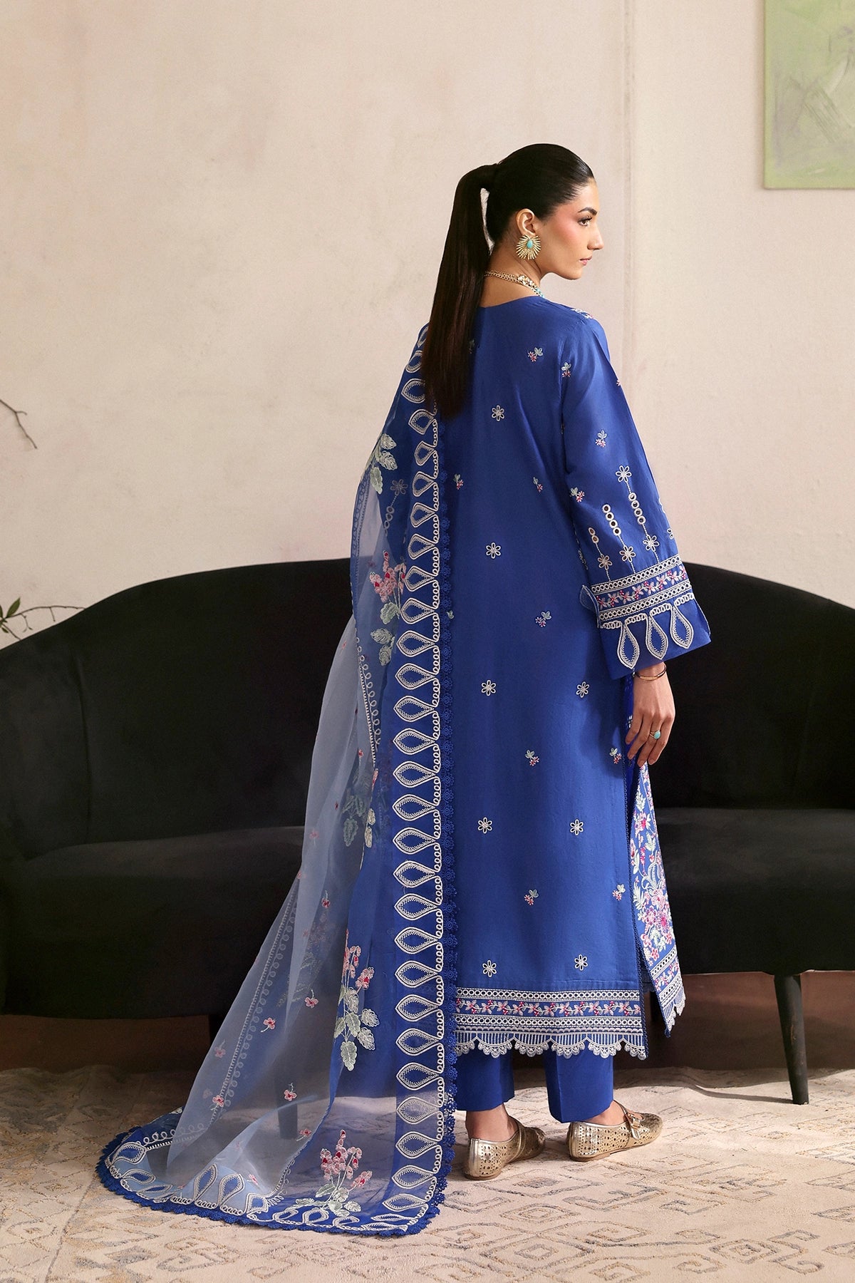 Woman in a blue embroidered outfit with a matching dupatta standing in a room.