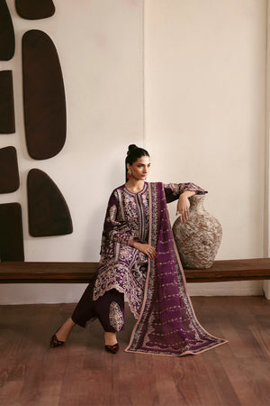 Woman in a purple and black traditional outfit sitting next to a decorative vase against a wall with abstract art.