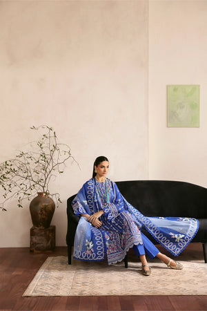 Woman in a blue patterned dress sitting on a black sofa in a room with a vase and plant.