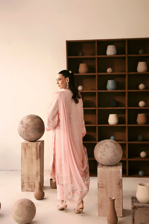 Woman in a light pink saree standing in a room with decorative spheres and shelves.