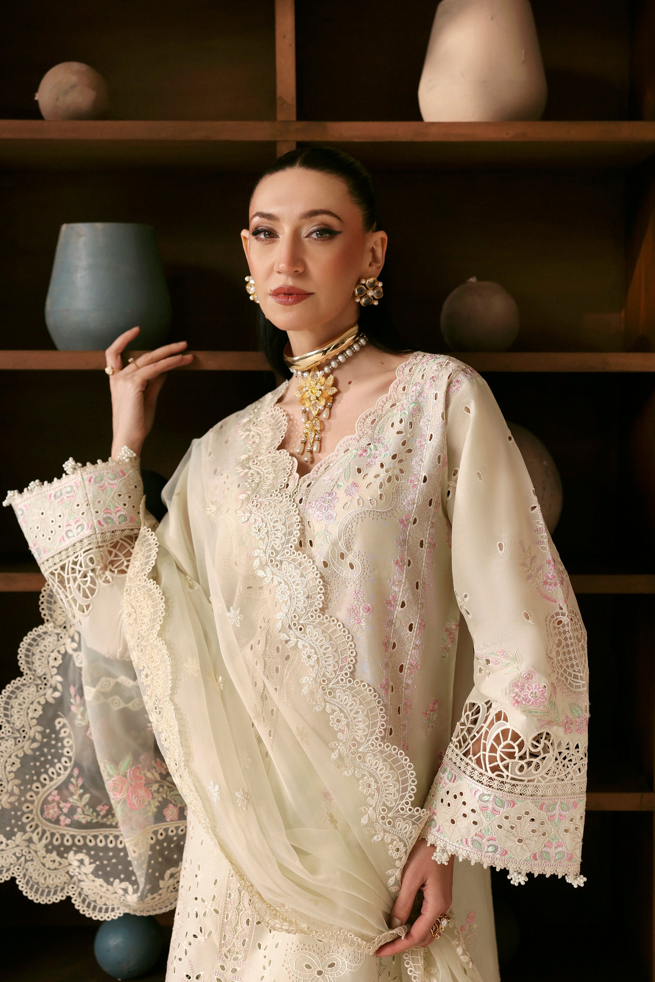 Woman wearing a cream-colored embroidered dress with a dark background