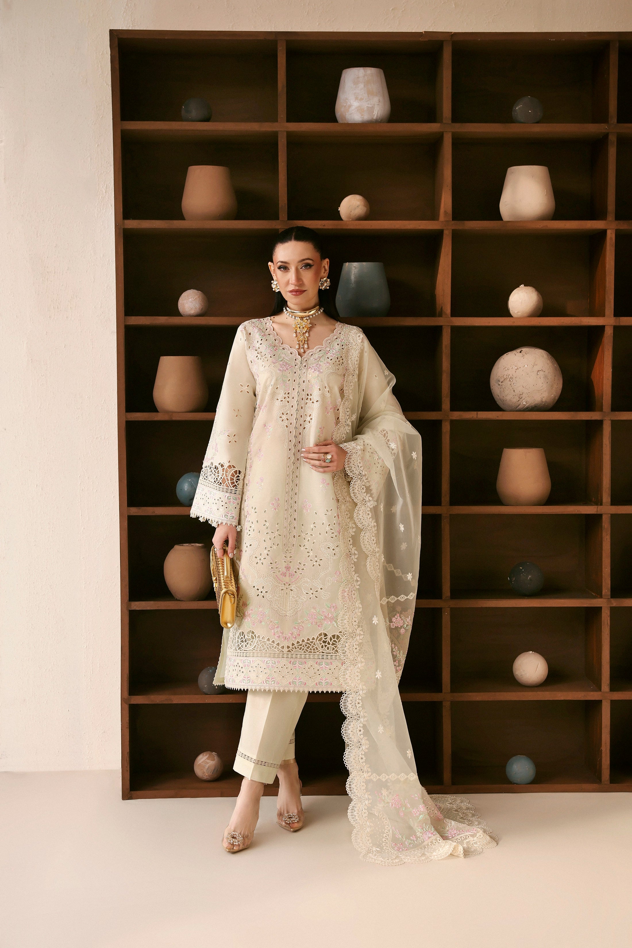 Woman in a white embroidered outfit standing in front of a bookshelf with decorative items.