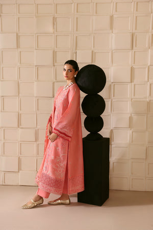 Woman in a pink traditional outfit standing next to a black decorative piece against a textured beige wall.