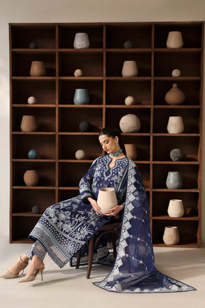 Woman in a blue patterned outfit sitting in front of a shelf with decorative pots.