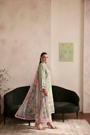 Woman in a light green traditional outfit standing in a room with a black sofa and a painting on the wall.