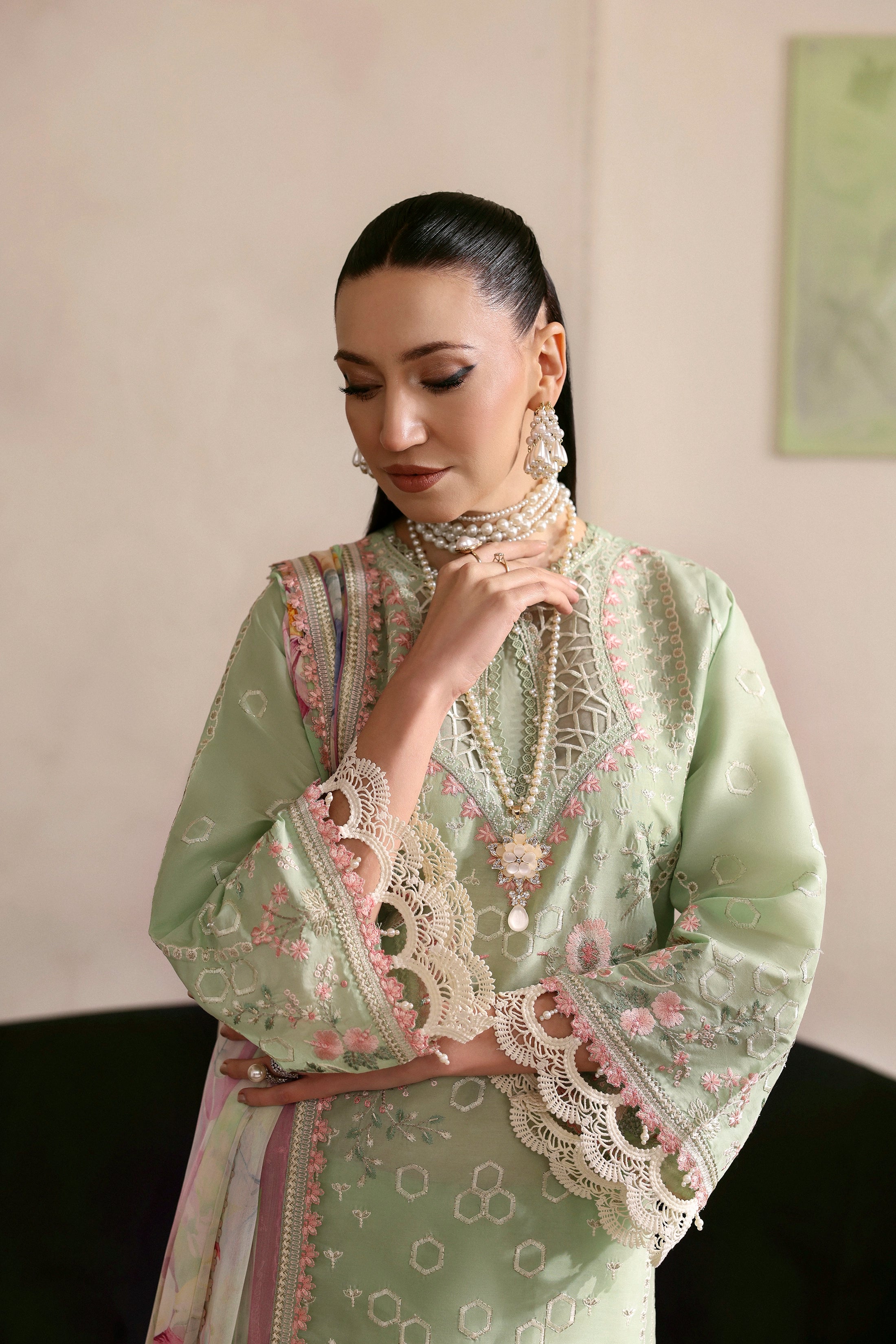 Woman wearing a light green embroidered traditional outfit with a plain background